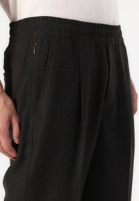 Pantalons de jogging noirs avec une taille élastique, poches latérales et une texture subtile ; comporte un petit accent de fermeture éclair à l'avant.