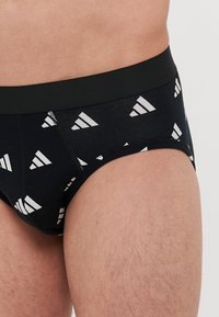 Crna donja rublja sa ponovljenim uzorkom bijelog trokutastog loga. Elastična traka oko struka je čvrsto crna.