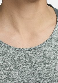 Camiseta verde jaspeada con cuello redondo, que presenta una tela suave y texturizada y un sutil detalle de logo en el área del lado izquierdo del pecho.