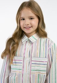 Csíkos gombos ing fehér színben, multicolor függőleges csíkokkal. Két mellzsebe, galléros nyakkivágás és könnyű textúra jellemzi.