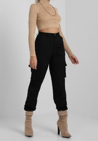 Pantalon cargo noir avec poches latérales, assorti à un crop top côtelé beige. Chaussures composées de bottes beige souples à talons.