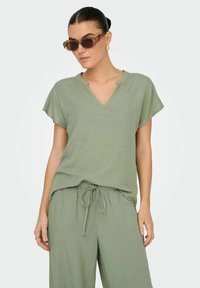 Ljusgrön tvådelad outfit med en lös, kortärmad topp med V-ringning och byxor med resår och snörning i midjan. Strukturerad tyg.