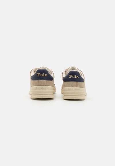Béžové semišové tenisky s námořníckym akcentom na päte a zlatým logom "Polo". Majú plochú podrážku a polstrovaný golier pre pohodlie a podporu.