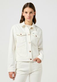 Vit denimjacka med krage, knappstängning och två bröstfickor. Har kopparfärgade knappar och en figursydd design.
