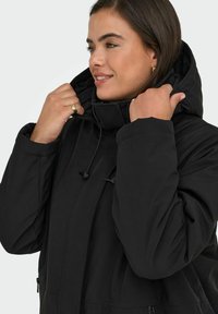 Svart vadderad jacka med hög krage och justerbar dragsko, med två sidofickor med dragkedja och en slät, matt yta.