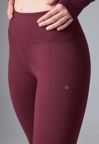 Bordowe legginsy wykonane z gładkiego, elastycznego materiału. Wysoki stan i subtelny detal z logo na lewym udzie. Bezszwowy design z eleganckim wykończeniem.