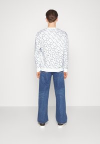 Camicia bianca a maniche lunghe con stampa del logo diagonale nera, abbinata a jeans blu a gamba larga. Design casual con polsini a costine in contrasto.