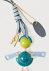 Privjesak za ključeve s plavim kožnim remenom, zlatnim lancem u obliku kuglica i šarenim okruglim plastičnim dijelovima u obliku stilizirane osobe koja drži male plave ručke.