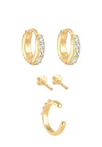 Pendientes de aro en tono dorado con cristales transparentes, dos pendientes de botón con detalles similares a perlas y un anillo abierto en tono dorado. Textura suave en todo.
