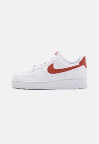 Fehér bőr sportcipő piros Nike swoosh-ral, textúrált gumi talppal és perforációkkal az orrán a légáteresztés érdekében. Klasszikus fűzőrendszer.