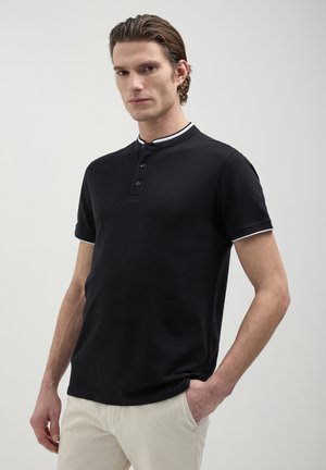 Polo shirt nera a maniche corte con patta a tre bottoni e dettagli bianchi sul colletto. Realizzata in tessuto di cotone testurizzato. Vestibilità regolare.
