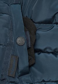 Navy puffer jacket fabric with quilted texture. Features black fleece lining, a round black button, and a brand label on a woven tag.