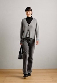 Pelēks ribots kardigans ar pogām, uzvilkts virs melnā turtlenecka, un apvienots ar pelēkiem platām biksēm. Izskatu papildina melna soma un zābaki.