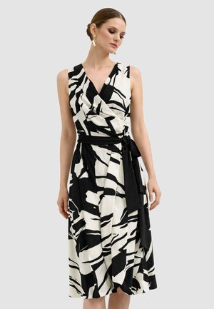 Donna che indossa un vestito avvolgente senza maniche con motivo astratto bianco e nero, cintura annodata in vita e orecchini dorati.