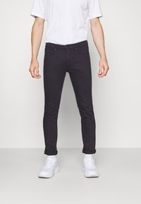 Vaqueros ajustados de color gris oscuro con cinco bolsillos, costuras resistentes y dobladillo enrollado, combinados con zapatillas blancas y una camiseta blanca lisa.