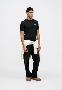 Czarna bawełniana koszulka z krótkim rękawem, w połączeniu z ciemnymi dżinsami i kremową bluzą zawiązaną w talii. Na nogach brązowe buty wsuwane.