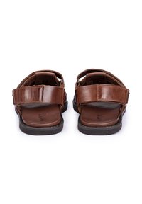 Braune Ledersandalen mit verstellbaren Riemen, offenem Rücken, flachen Sohlen und kontrastierenden Nähten. Sie verfügen über eine strukturierte Oberfläche und sind robust gebaut.