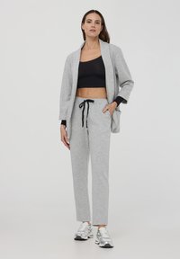 Outfit casual grigio chiaro con un cardigan lungo e pantaloni abbinati. Il cardigan ha maniche larghe; i pantaloni hanno una vita con cordino.