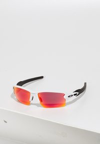 Okulary przeciwsłoneczne z białą ramką i czarnymi akcentami, wyposażone w czerwone gradientowe soczewki. Sportowy design, lekkie z zakrzywionymi ramionami. 