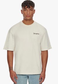 Beige Baumwoll-T-Shirt mit kurzen Ärmeln, Rundhalsausschnitt und in Schwarz auf der linken Brust eingesticktem "Dropsize"-Text. Entspanntes Passformdesign.