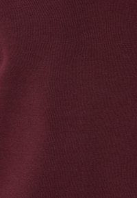 Bordeaux katoen stof met een gladde textuur, met subtiele variaties in tint en een zachte, rekbare feel.
