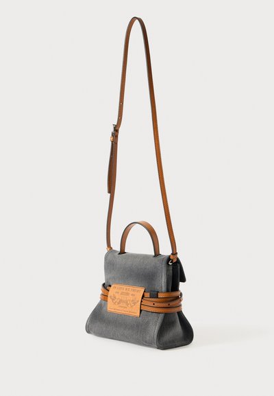 Bolsa de tecido cinza com uma alça e detalhes em couro castanho, apresentando uma pequena pega no topo e um rótulo retangular em couro na frente.