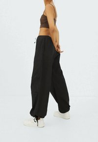 Pantalon noir ample avec une taille élastique et un cordon de serrage, confectionné dans un tissu léger. Porté avec des baskets blanches.