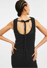 Robe en crochet noir avec un dos dégagé agrémenté d'un détail à nouer, texture côtelée et silhouette ajustée.