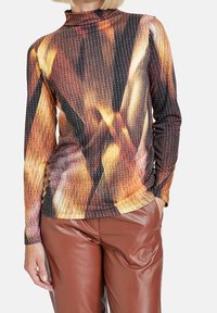 T-shirt à manches longues avec un col haut, présentant un motif multicolore dans les tons orange, marron et noir. Fabriqué en tissu texturé et extensible.