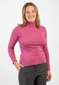 Maglione a maniche lunghe con collo alto di un vivace colore rosa, realizzato in tessuto elastico. Texture liscia con silhouette aderente e cuciture minime. Abbinato a pantaloni grigi.