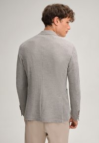 Grau gemusterter Blazer aus strukturiertem Stoff, mit Reverskragen und geknöpften Manschetten, der eine taillierte Passform und einen Rückenschlitz aufweist.