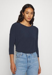 Marineblå langermet topp med avslappet passform og utringet hals, kombinert med høyhårede lyseblå jeans. Glatt tekstur, minimalistisk design.