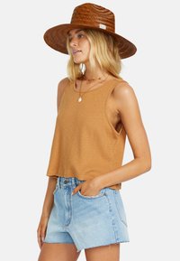 Brown ribbed crop tank top paired with light blue denim shorts. Model wears a wide-brimmed straw hat and layered necklaces.