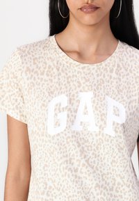Bežinė leopardų rašto marškinėliai su balta "GAP" logotipu. Trumpomis rankovėmis ir apvaliu iškirpimu, pasižymintys minkšta medvilnės tekstūra.
