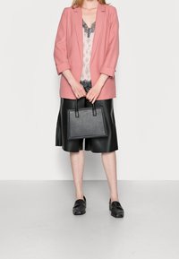 Pink blazer over a lace-trimmed top, paired with a black leather skirt and loafers. Holds a small black handbag.