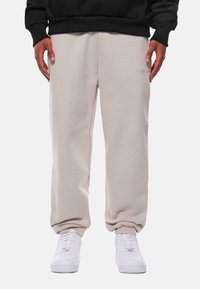 Lys beige sweatpants med en afslappet pasform, lavet af blødt stof. Har et lille broderet logo og ribbede ankler. Båret med hvide sneakers.