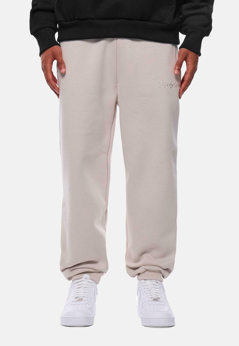 Lys beige sweatpants med en afslappet pasform, lavet af blødt stof. Har et lille broderet logo og ribbede ankler. Båret med hvide sneakers.