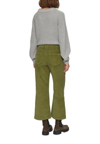 Grüne Cordhosen mit weitem Bein und strukturierter Oberfläche, kombiniert mit einem hellgrauen Strickpullover und braunen Knöchelstiefeln. Sichtbare Gesäßtaschen.
