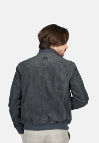Pánská tmavě šedá semišová bomber bunda s žebrovaným límcem, strukturovaným povrchem, elastickým páskem a diskrétním logem na zadní straně.