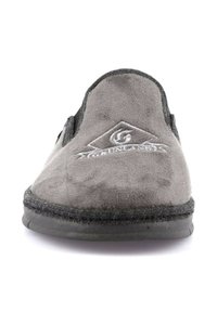 Pantofola in suede grigia con punta arrotondata, caratterizzata da una superficie testurizzata e un logo ricamato sulla parte anteriore. Bordo nero e suola flessibile.