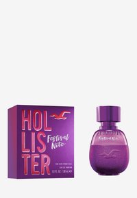 Hollister Festival Nite Parfum, 30 ml, besticht durch eine runde, glitzernde lila Flasche mit einem zylindrischen Deckel und einer passenden lila Schachtel.
