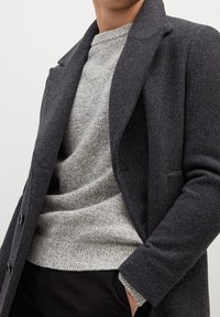 Manteau en laine charbon à coupe ajustée, revers à cran et poches latérales, superposé à un pull en tricot gris clair. Texture lisse, design moderne.