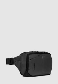 Marsupio nero in nylon con pannelli testurizzati e lisci, forma rettangolare, chiusura con cerniera e cinturino regolabile con fibbia.