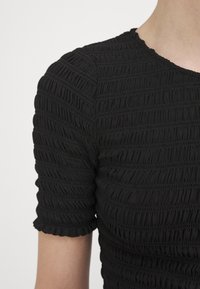Top nero con maniche corte arricciate. Presenta un tessuto testurizzato ed elasticizzato con dettagli di smocking orizzontale e scollatura rotonda.