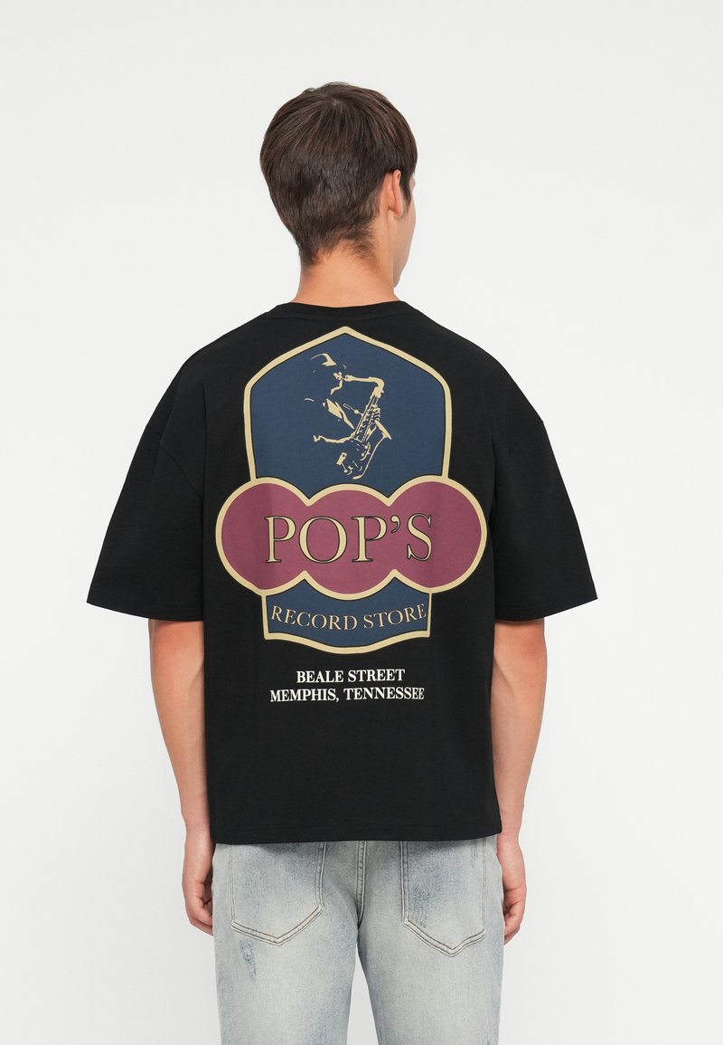 Black T-shirt featuring a large graphic in gold, red, and blue on the back, displaying "POP'S RECORD STORE" and a saxophonist illustration.