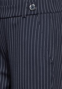 Pantalons rayés bleu marine en tissu léger ; dotés d'une poche avant et d'une fermeture à bouton avec un fil contrasté.