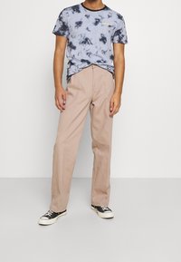 Camiseta azul claro de tie-dye con ribetes negros, combinada con pantalones rectos beige y zapatillas negras con suelas blancas.