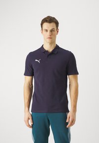 Marineblaues Poloshirt mit kurzen Ärmeln, auf dessen linker Brust sich ein weißes Puma-Logo befindet. Es besteht aus Baumwolle, hat einen klassischen Kragen und eine glatte Textur.