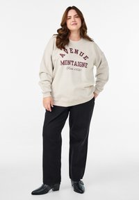 Svetlobežový svetrom so vzorom "Avenue Montaigne" vytlačeným v bordovej, spárovaný s čiernymi širokými nohavicami a čiernymi členkovými topánkami na opätku.