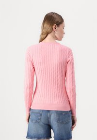 Rosa strikket genser med kabelmønster, rund hals, tettsittende lange ermer og ribbestrikket hem, kombinert med blå denimshorts.